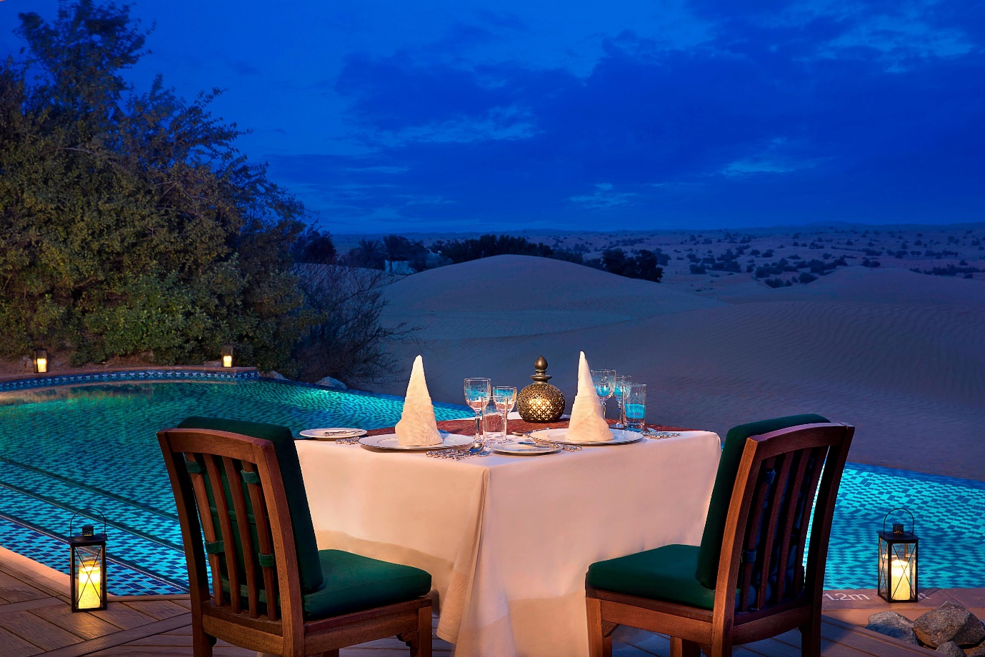 a dinner table for two people set besides the swimming pool of the Al Maha Resort that’s in between a desert in Dubai | Wedifys