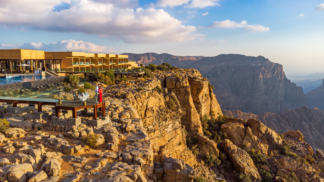 a couple standing in the balcony of the Anantara Al Jabal Akhdar Resort looking down the mountain | Wedifys