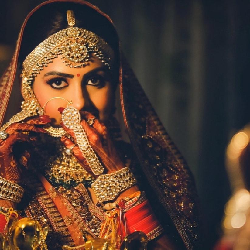 a traditional Indian bride adorning beautiful jewelry and nath | Wedifys