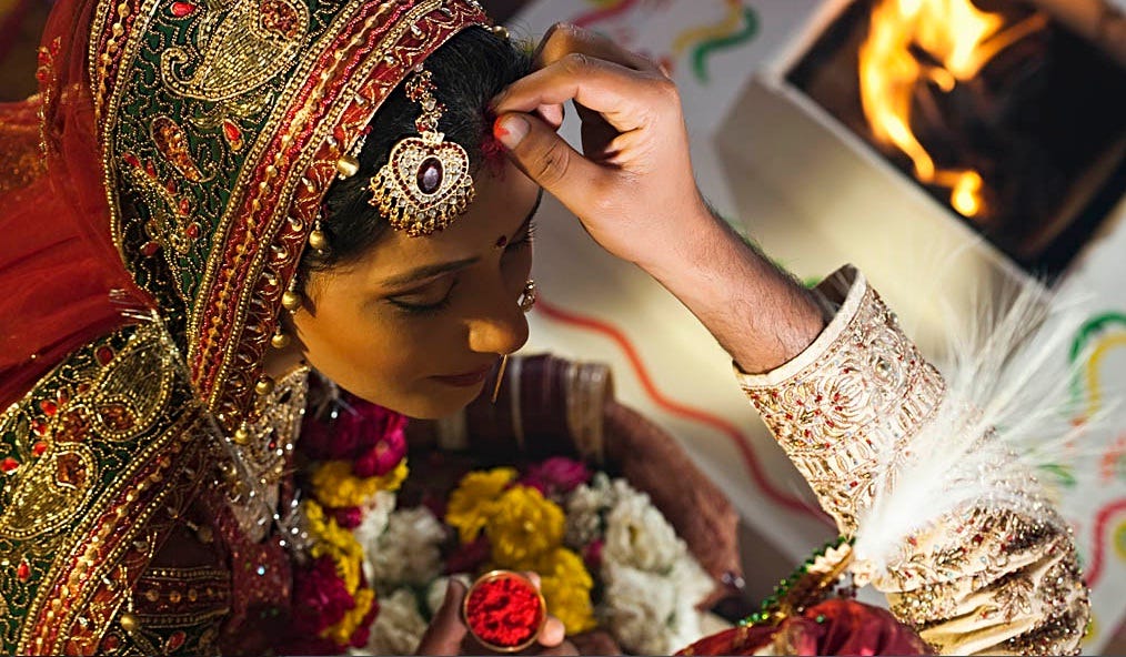 groom putting sindoor in his wife’s hair as part of the wedding ceremony ritual | Wedifys